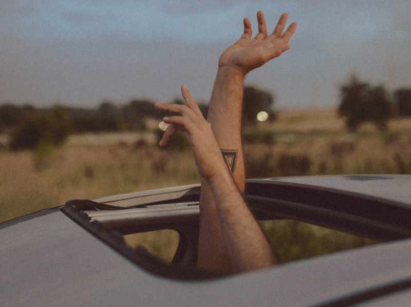 Zwei Hände winken aus dem geöffneten Schiebedach eines Autos