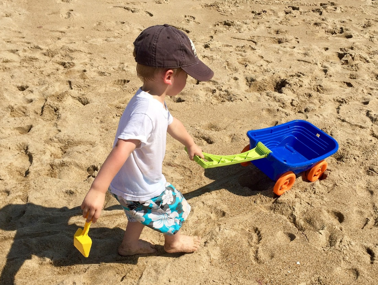 Ein Junge spielt mit einer Schaufel und einer Schubkarre am Strand