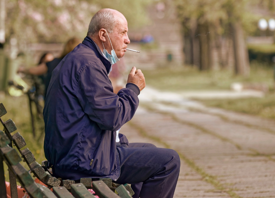 Ein alter Mann sitzt auf einer Parkbank und raucht eine Zigarette