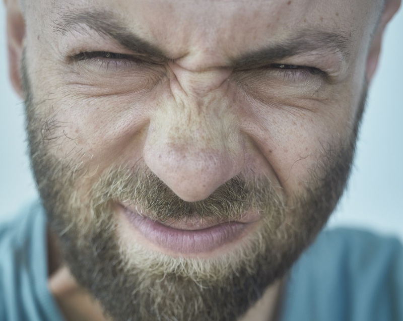 Ein Mann mit Bart verzieht das Gesicht und kneift die Augen zusammen