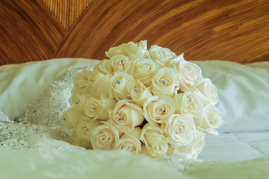 Ein Blumenstrauß mit weißen Rosen liegt auf dem weißen Laken eines Bettes.