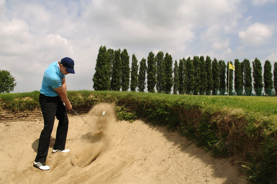 Ein Golfspieler macht einen Abschlag in einem Sandbunker.