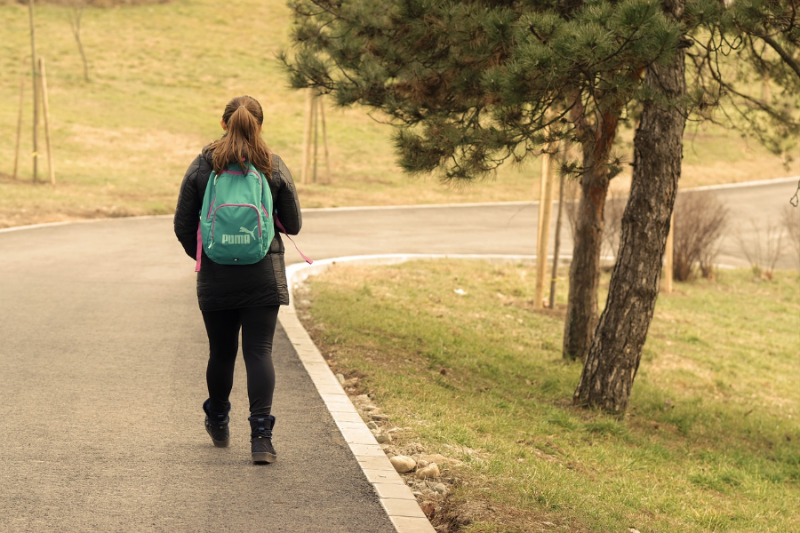 Ein Mädchen mit einem grünen Rucksack läuft am Rand einer Landstraße entlang.