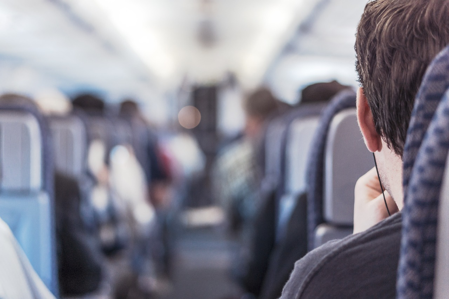 Ein Passagier sitz im Mittelgang eines Flugzeugs und hat Kopfhörer im Ohr.