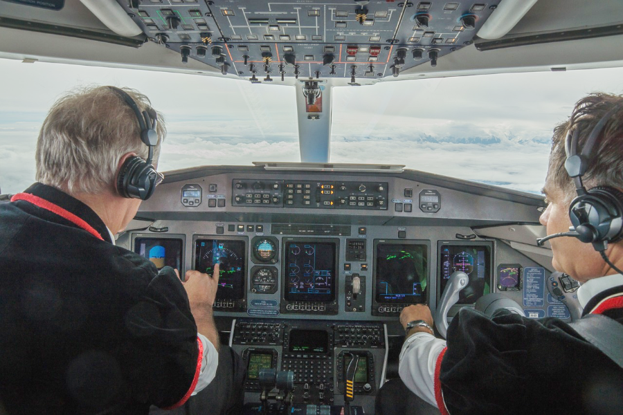 Zwei Piloten mit grauen Haaren sitzen im Cockpit eines Flugzeugs und steuern die Maschine.