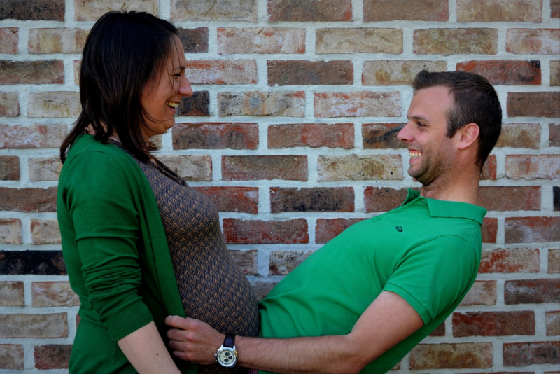 Eine lachende schwangere Frau hält ihren Bauch an den Bauch ihres Mannes.