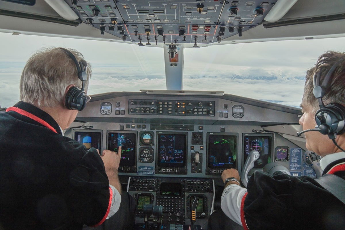 Zwei Piloten mit grauen Haaren sitzen im Cockpit eines Flugzeugs und steuern die Maschine.