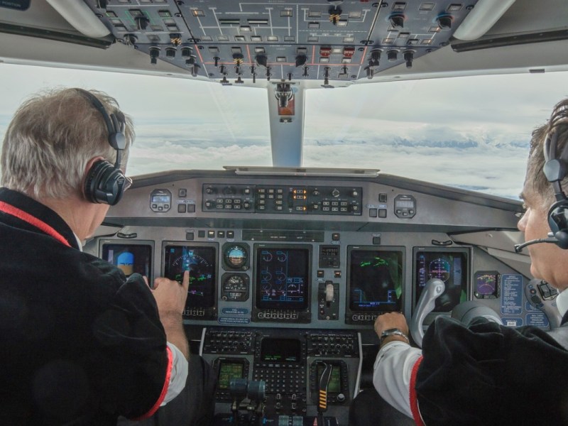 Zwei Piloten mit grauen Haaren sitzen im Cockpit eines Flugzeugs und steuern die Maschine.