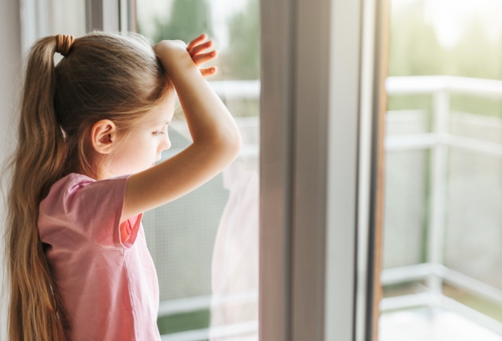 Ein kleines Mädchen steht am Fenster.