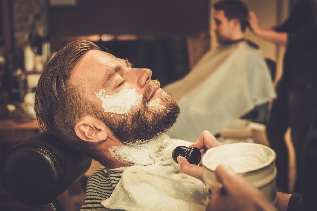 Ein Mann wird bei einem Barbier mit Rasierschaum im Gesicht bedeckt.