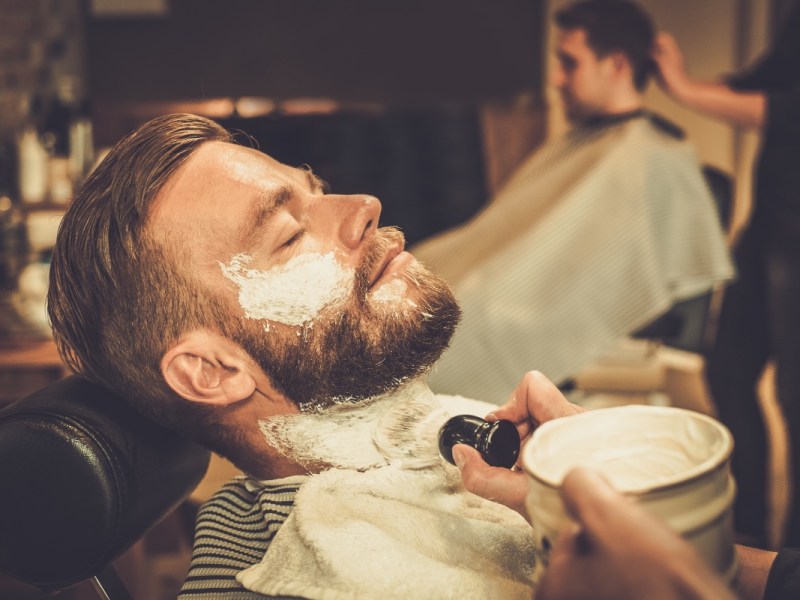 Ein Mann wird bei einem Barbier mit Rasierschaum im Gesicht bedeckt.