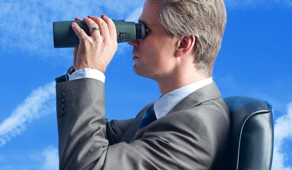 Ein Geschäftsmann schaut mit einem Fernglas in den blauen Himmel.