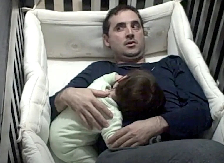 Ein Vater liegt neben seiner schlafenden Tochter im Baby-Bett.