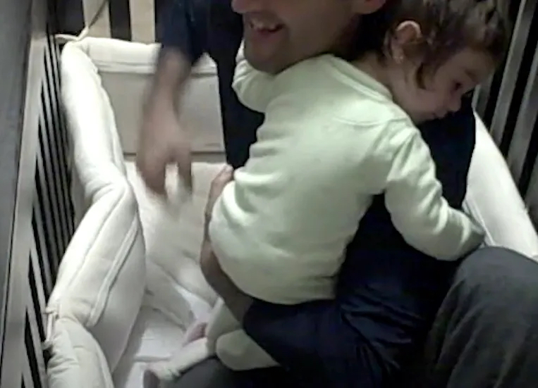 Ein Vater hält seine kleine Tochter in einem Baby-Bett im Arm.