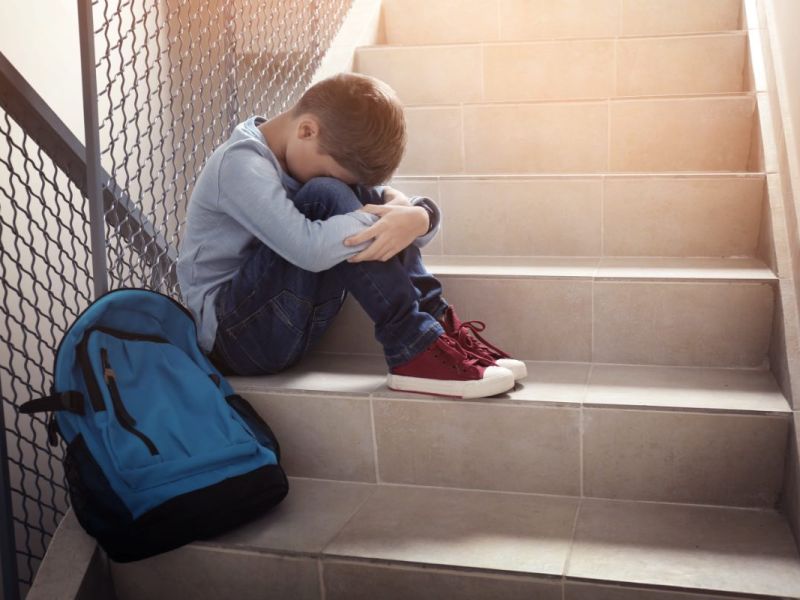 Ein trauriger Junge sitzt im Treppenhaus einer Schule.
